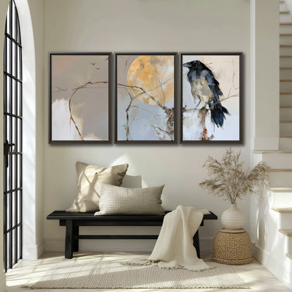 A dark raven beside a golden moon amid pale blue and cream painterly strokes 3 piece framed canvas wall art displayed in a entryway