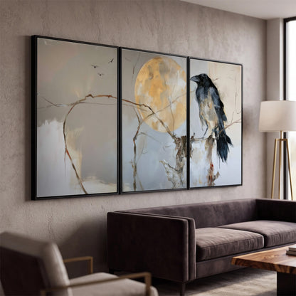 A dark raven beside a golden moon amid pale blue and cream painterly strokes 3 piece framed canvas wall art displayed in a modern living room