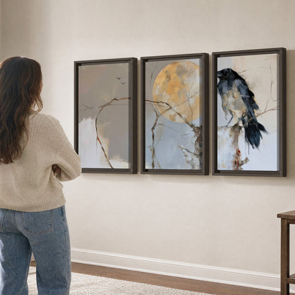 A dark raven beside a golden moon amid pale blue and cream painterly strokes 3 piece framed canvas wall art three panel arrangement on a wall