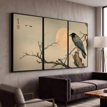A dark raven perched on a bare branch beside a warm full moon 3 piece framed canvas wall art displayed in a modern living room