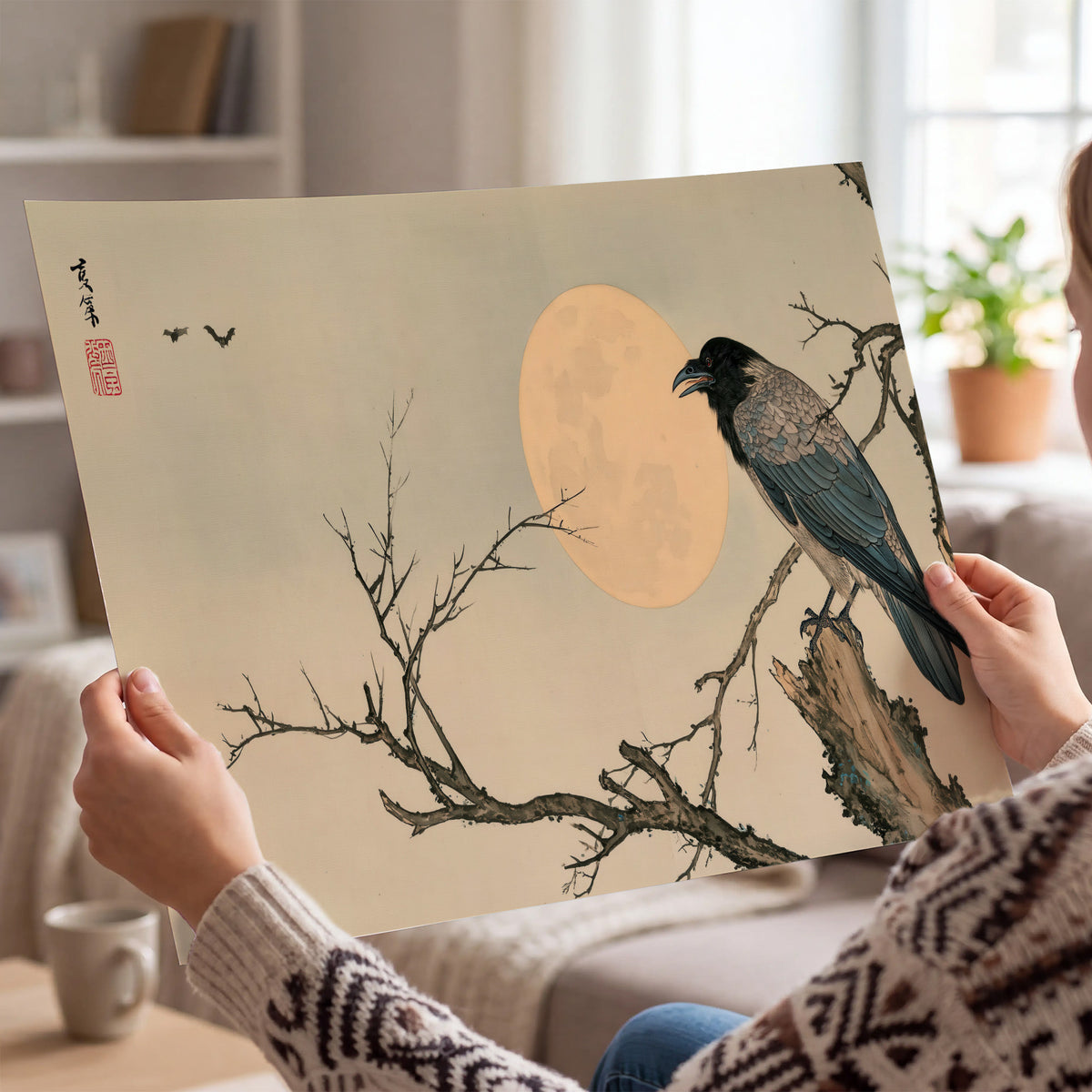 A dark raven perched on a bare branch beside a warm full moon single poster print held in hands