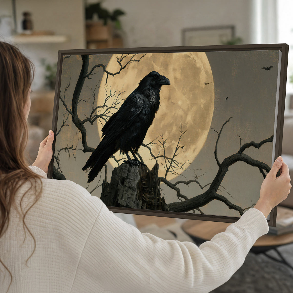 A black raven standing among bare branches in front of a large golden moon single framed canvas wall art held in hands