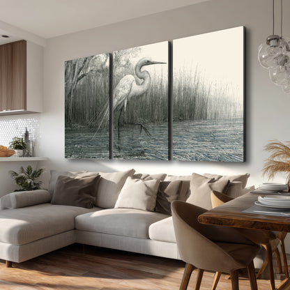 A pale long-legged heron standing beside tall reeds in a muted gray-green wetland 3 piece canvas wall art room and product view