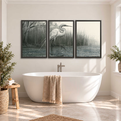 A pale long-legged heron standing beside tall reeds in a muted gray-green wetland 3 piece framed canvas wall art styled in an interior
