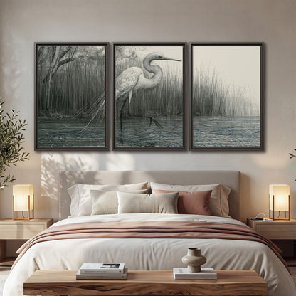 A pale long-legged heron standing beside tall reeds in a muted gray-green wetland 3 piece framed canvas wall art displayed in a bedroom