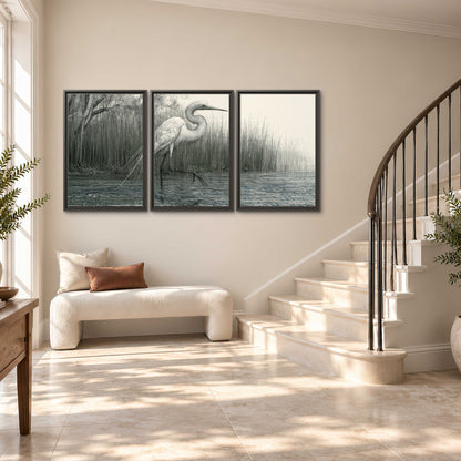 A pale long-legged heron standing beside tall reeds in a muted gray-green wetland 3 piece framed canvas wall art styled in an interior