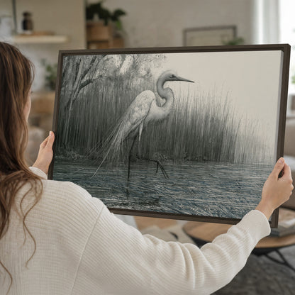 A pale long-legged heron standing beside tall reeds in a muted gray-green wetland single framed canvas wall art held in hands