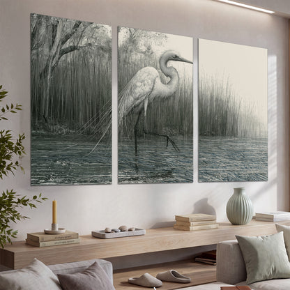 A pale long-legged heron standing beside tall reeds in a muted gray-green wetland set of 3 poster prints displayed in a console