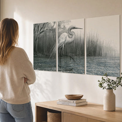 A pale long-legged heron standing beside tall reeds in a muted gray-green wetland set of 3 poster prints three panel arrangement on a wall