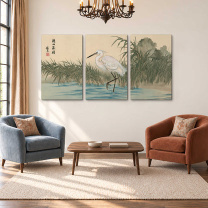 A white heron standing beside a quiet river with reeds and distant hills 3 piece canvas wall art styled in an interior