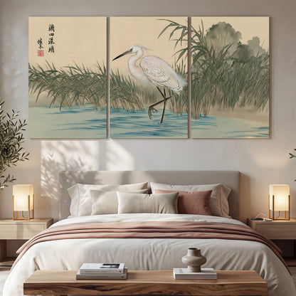 A white heron standing beside a quiet river with reeds and distant hills 3 piece canvas wall art displayed in a bedroom