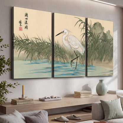 A white heron standing beside a quiet river with reeds and distant hills 3 piece canvas wall art displayed in a console