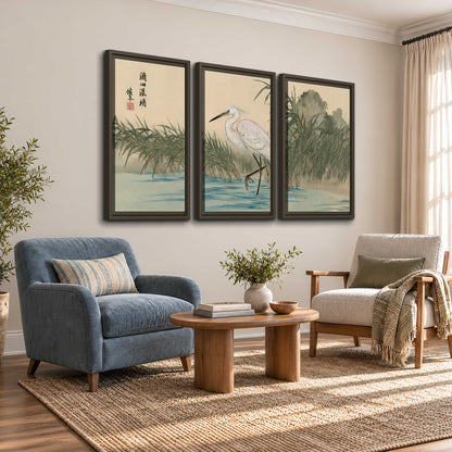 A white heron standing beside a quiet river with reeds and distant hills 3 piece framed canvas wall art styled in an interior