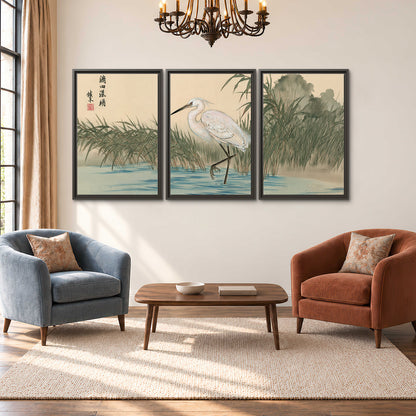 A white heron standing beside a quiet river with reeds and distant hills 3 piece framed canvas wall art styled in an interior