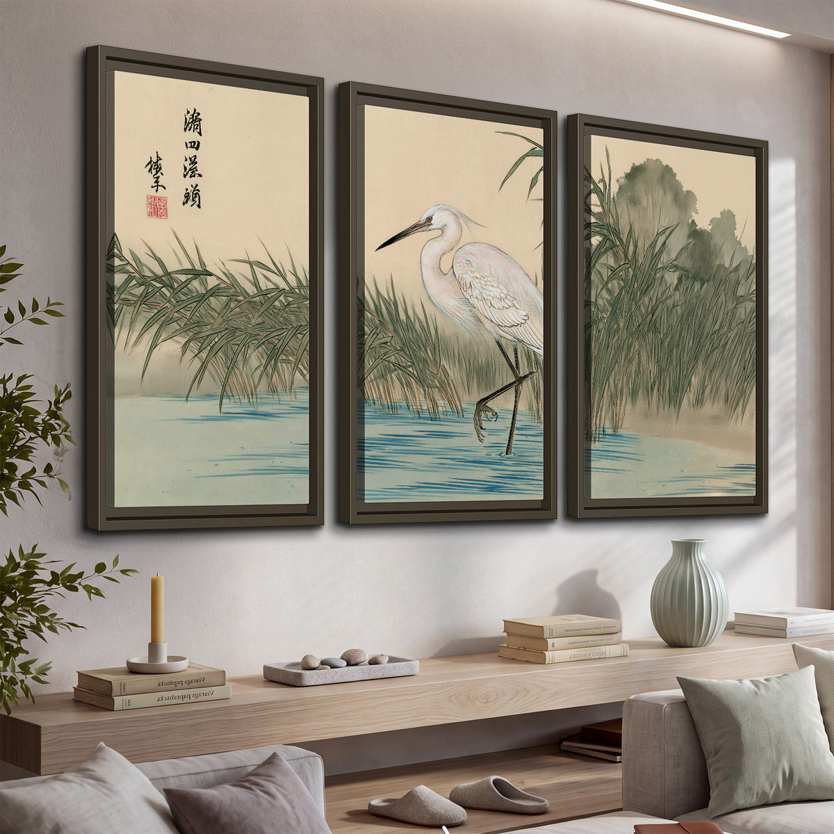 A white heron standing beside a quiet river with reeds and distant hills 3 piece framed canvas wall art displayed in a console