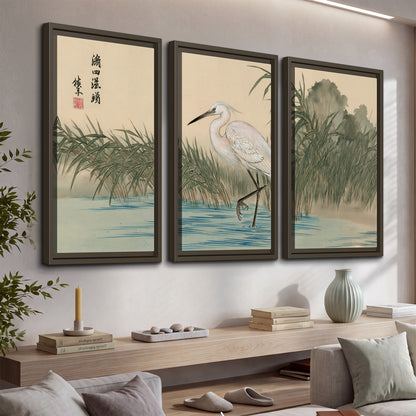 A white heron standing beside a quiet river with reeds and distant hills 3 piece framed canvas wall art displayed in a console