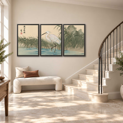 A white heron standing beside a quiet river with reeds and distant hills 3 piece framed canvas wall art styled in an interior