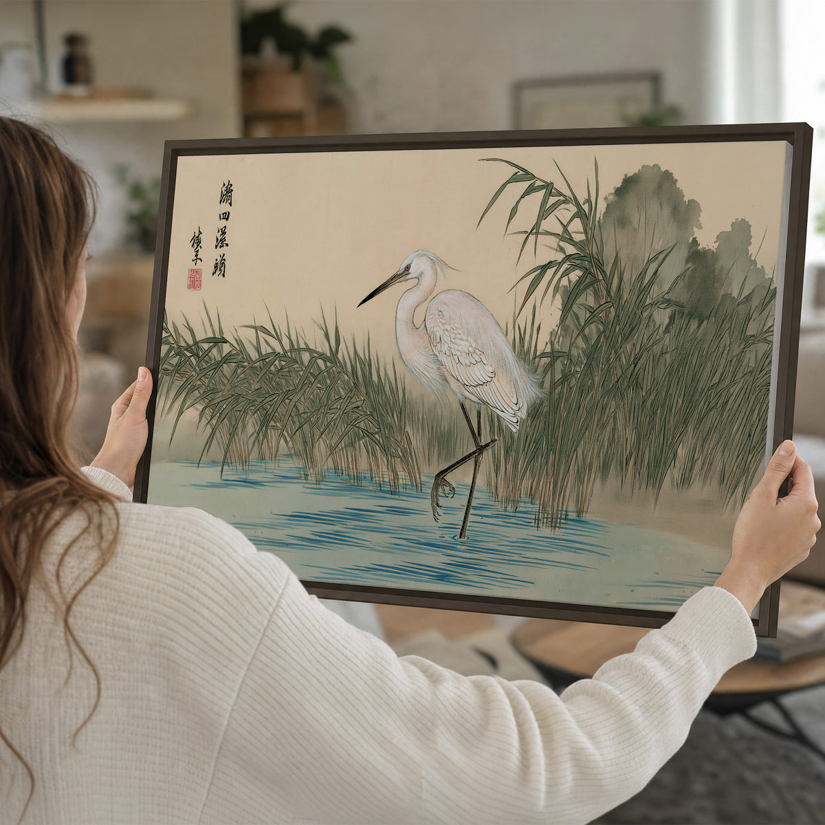 A white heron standing beside a quiet river with reeds and distant hills single framed canvas wall art held in hands