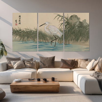 A white heron standing beside a quiet river with reeds and distant hills set of 3 poster prints displayed in a living room