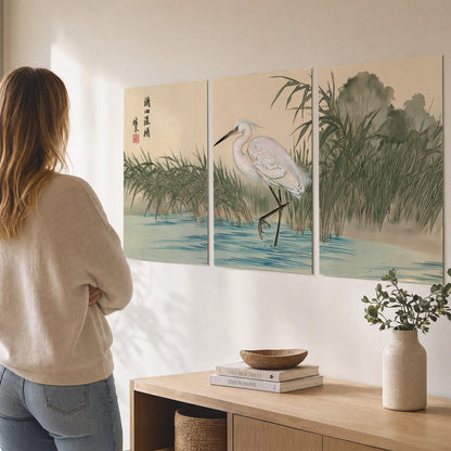 A white heron standing beside a quiet river with reeds and distant hills set of 3 poster prints three panel arrangement on a wall