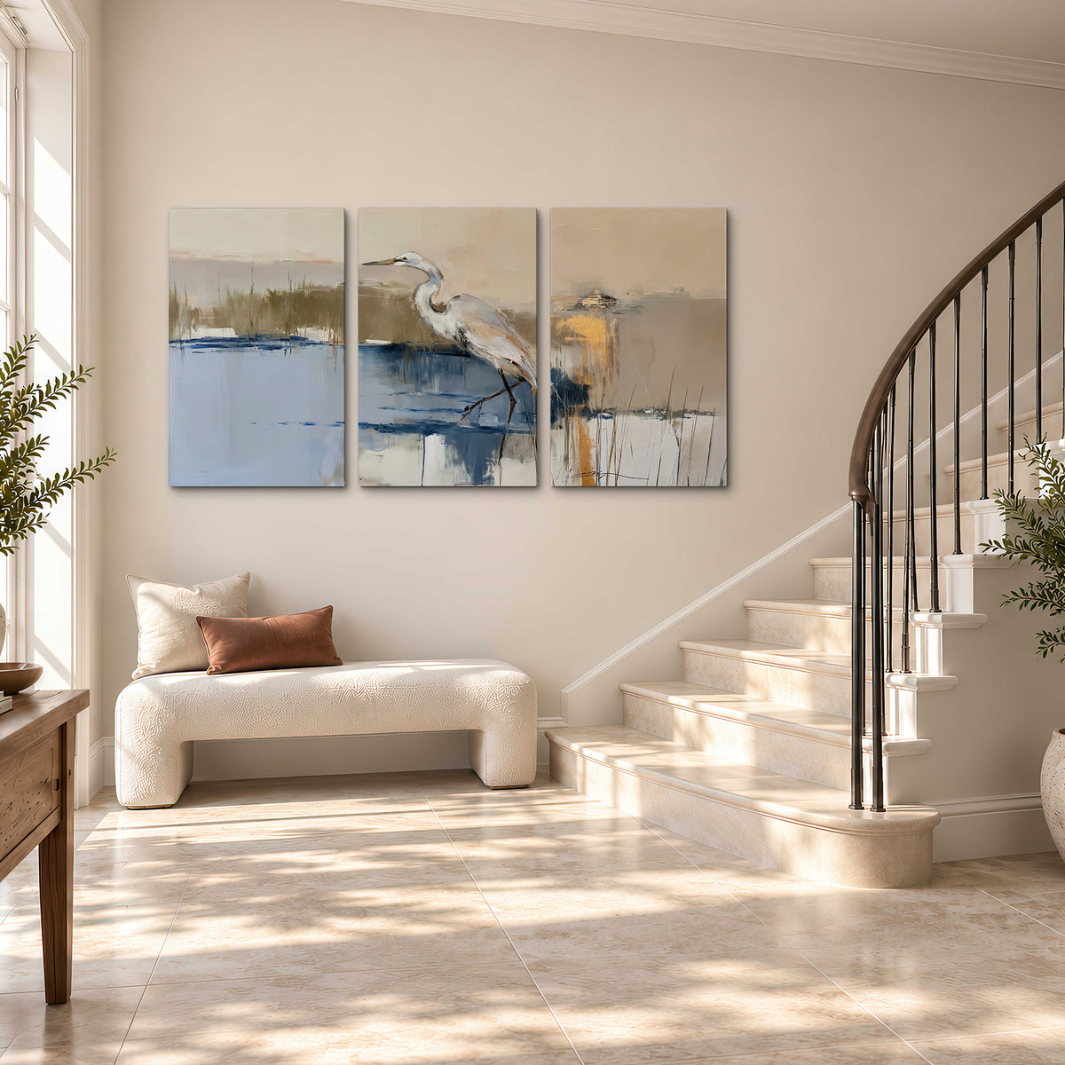 A slender heron standing in blue water among loose ochre and cream brushstrokes 3 piece canvas wall art styled in an interior