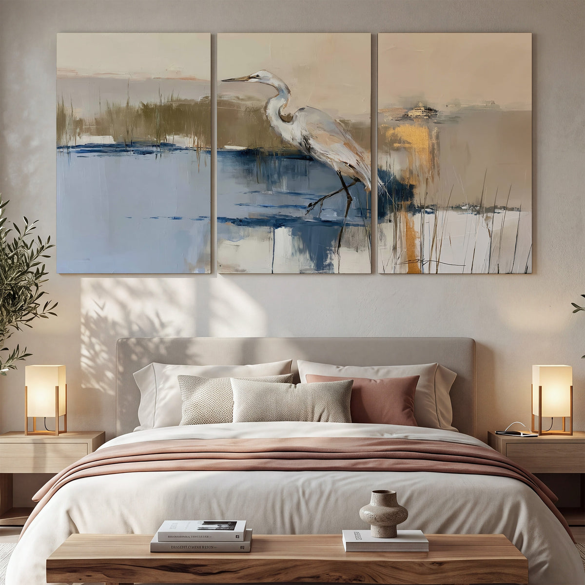 A slender heron standing in blue water among loose ochre and cream brushstrokes 3 piece canvas wall art displayed in a bedroom
