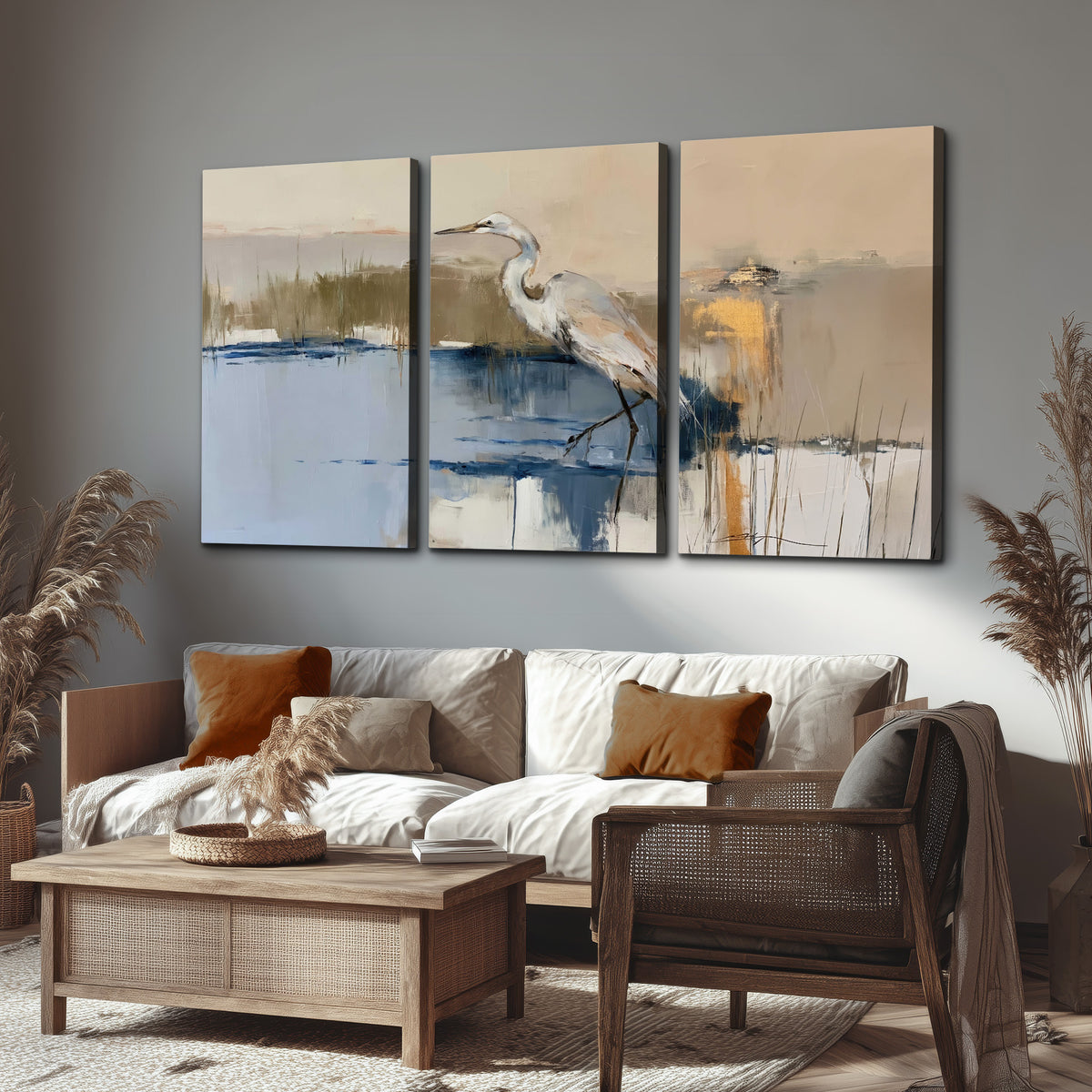 A slender heron standing in blue water among loose ochre and cream brushstrokes 3 piece canvas wall art displayed in a rustic living room