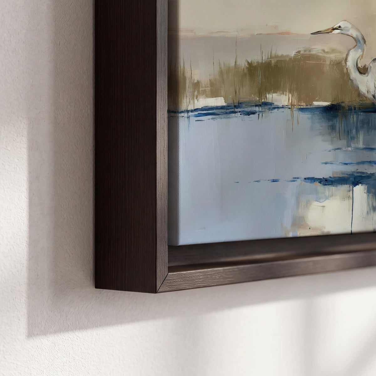 A slender heron standing in blue water among loose ochre and cream brushstrokes 3 piece framed canvas wall art material and edge close up