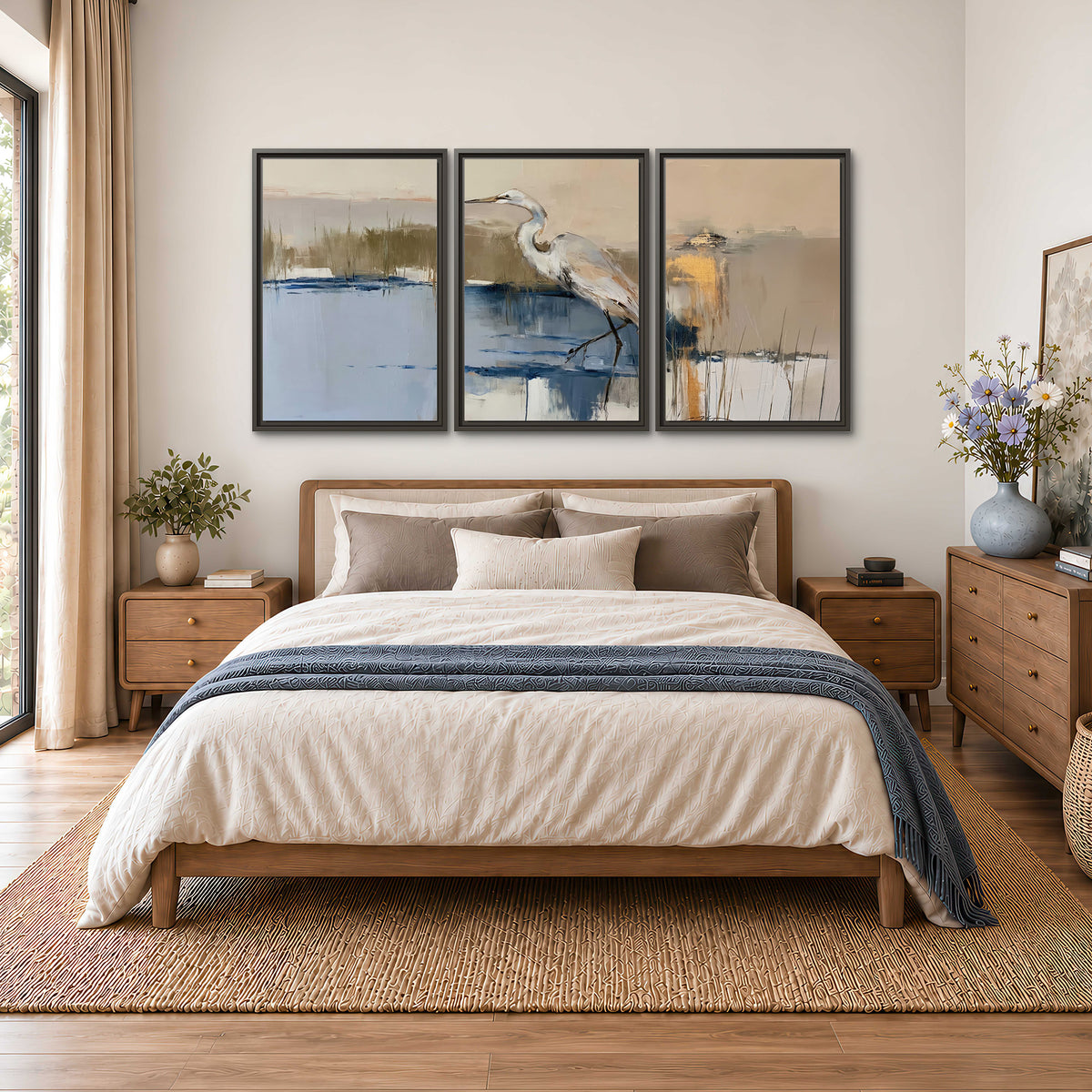 A slender heron standing in blue water among loose ochre and cream brushstrokes 3 piece framed canvas wall art styled in an interior