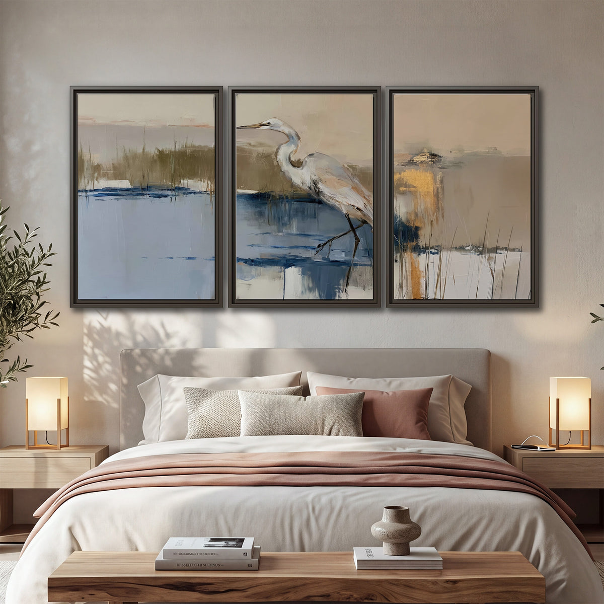 A slender heron standing in blue water among loose ochre and cream brushstrokes 3 piece framed canvas wall art displayed in a bedroom