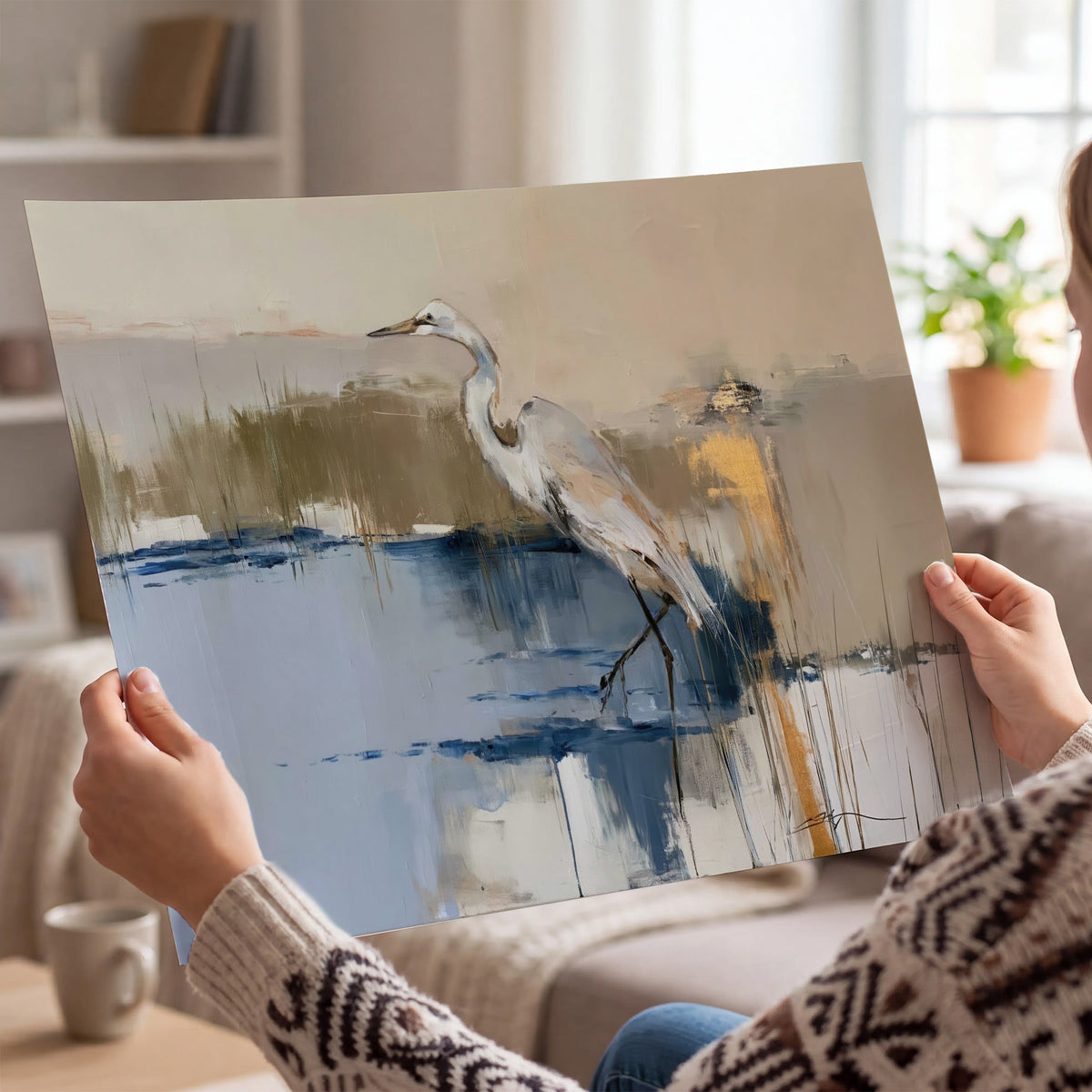 A slender heron standing in blue water among loose ochre and cream brushstrokes single poster print held in hands
