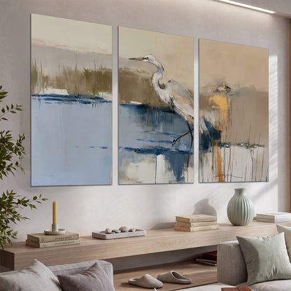 A slender heron standing in blue water among loose ochre and cream brushstrokes set of 3 poster prints displayed in a console