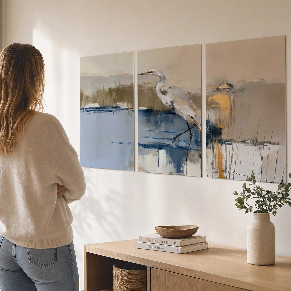 A slender heron standing in blue water among loose ochre and cream brushstrokes set of 3 poster prints three panel arrangement on a wall