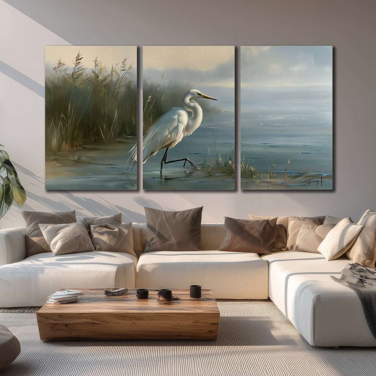 A white heron beside tall marsh grasses and still blue water 3 piece canvas wall art displayed in a living room