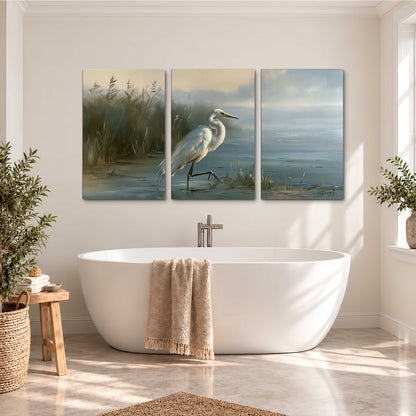 A white heron beside tall marsh grasses and still blue water 3 piece canvas wall art styled in an interior