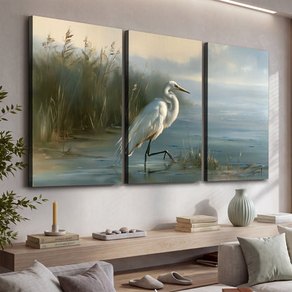 A white heron beside tall marsh grasses and still blue water 3 piece canvas wall art displayed in a console