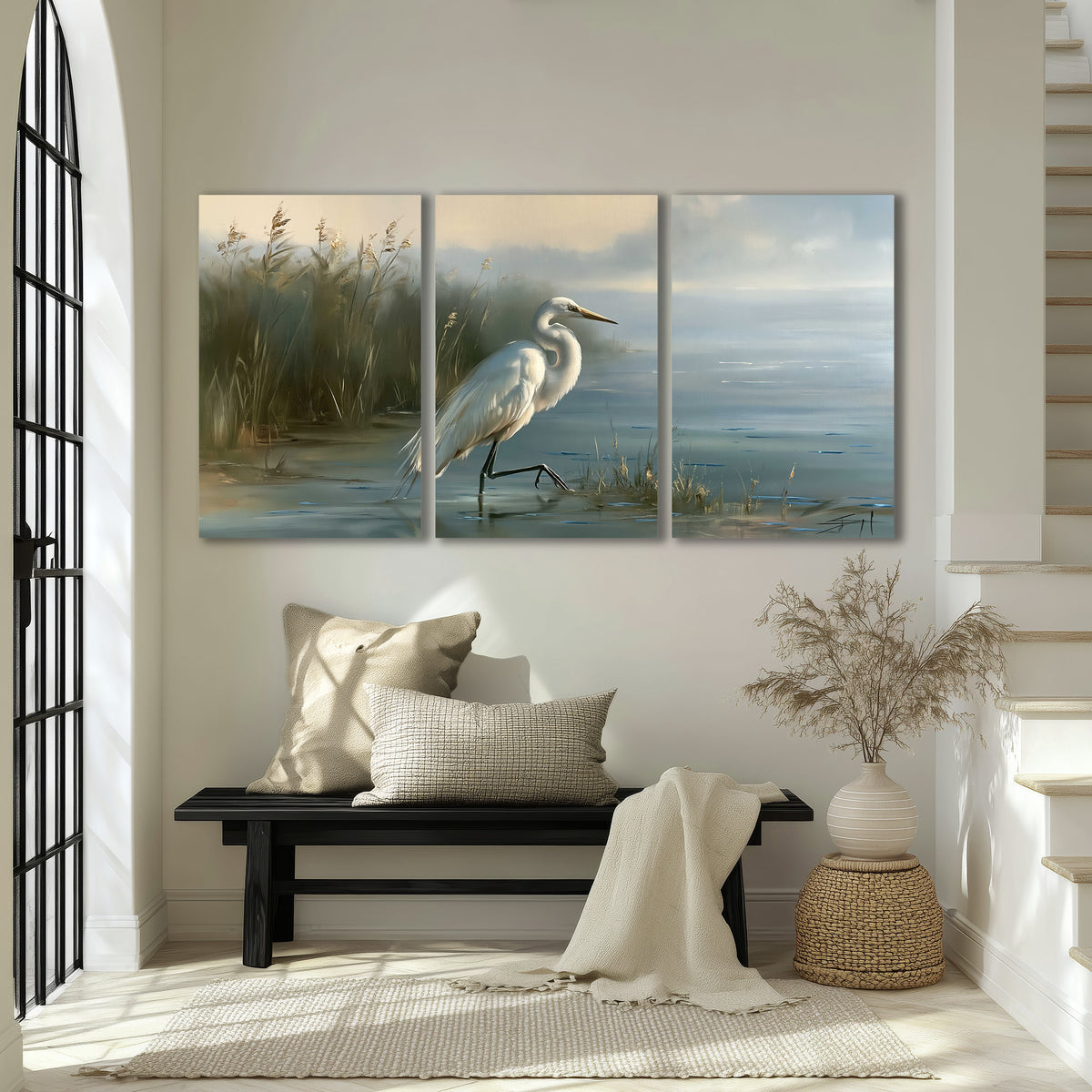 A white heron beside tall marsh grasses and still blue water 3 piece canvas wall art displayed in a entryway