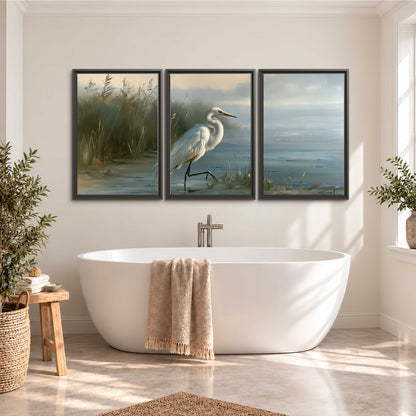 A white heron beside tall marsh grasses and still blue water 3 piece framed canvas wall art styled in an interior