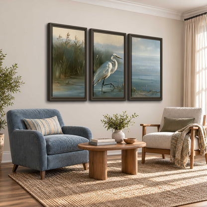 A white heron beside tall marsh grasses and still blue water 3 piece framed canvas wall art styled in an interior