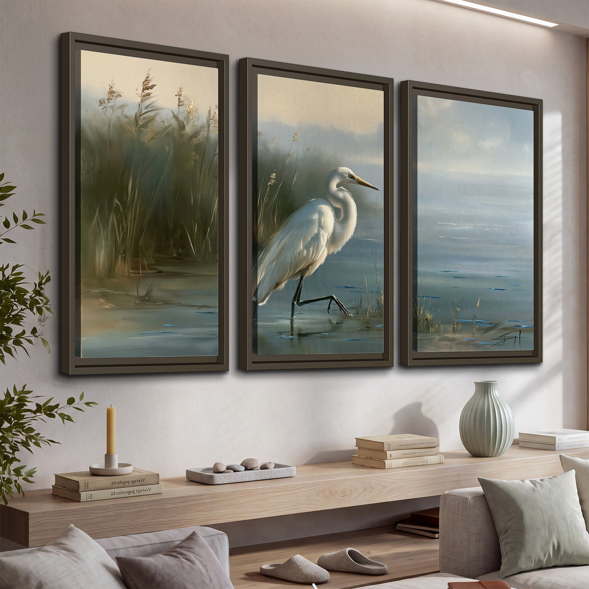 A white heron beside tall marsh grasses and still blue water 3 piece framed canvas wall art displayed in a console