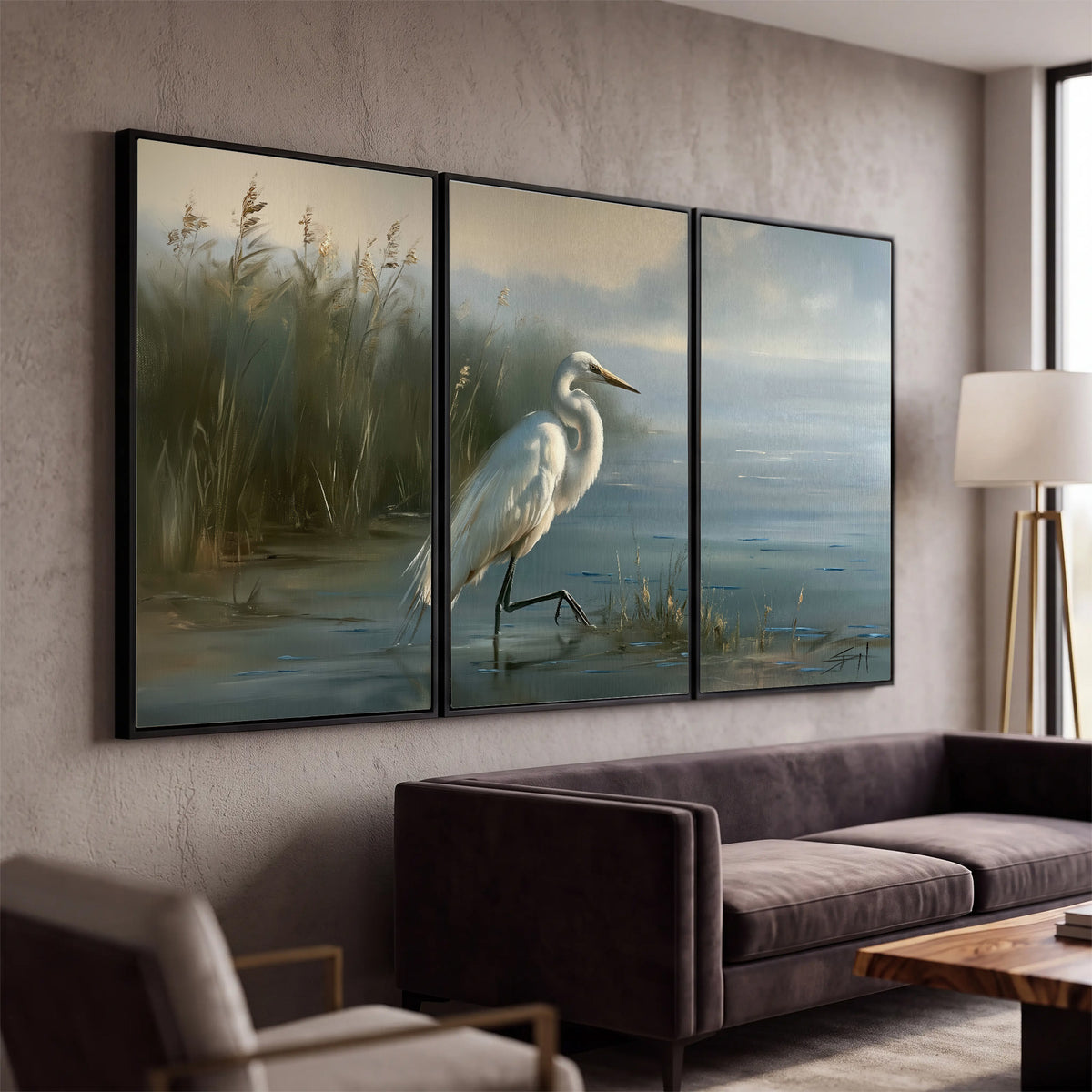 A white heron beside tall marsh grasses and still blue water 3 piece framed canvas wall art displayed in a modern living room