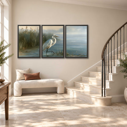 A white heron beside tall marsh grasses and still blue water 3 piece framed canvas wall art styled in an interior