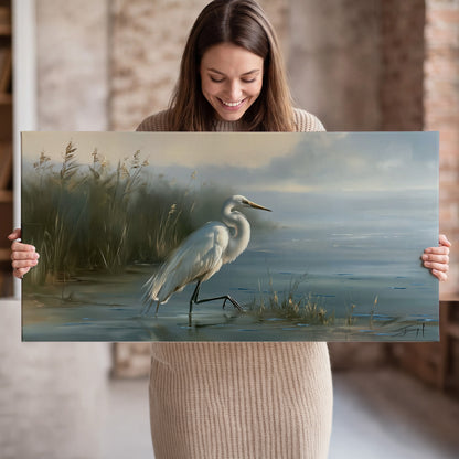 A white heron beside tall marsh grasses and still blue water single canvas wall art held in hands