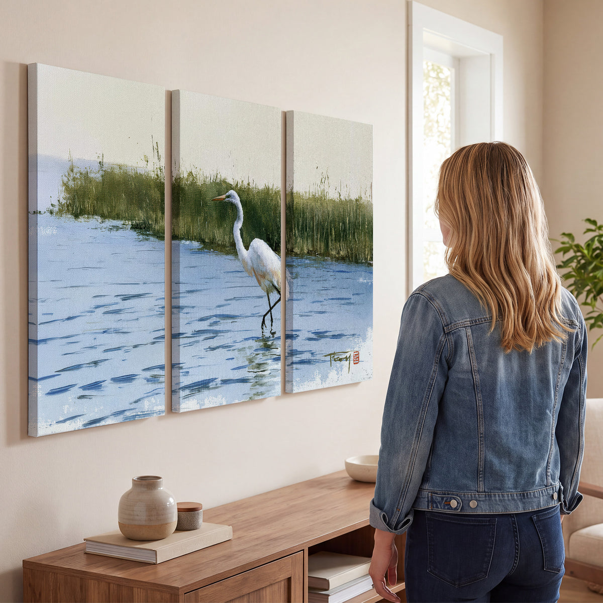 A white heron wading through bright blue water beside green reeds 3 piece canvas wall art three panel arrangement on a wall