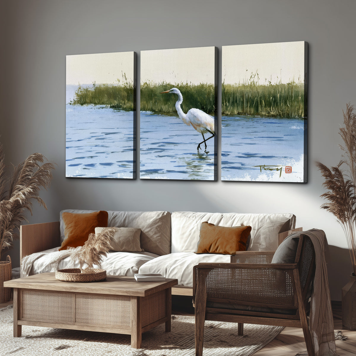 A white heron wading through bright blue water beside green reeds 3 piece canvas wall art displayed in a rustic living room