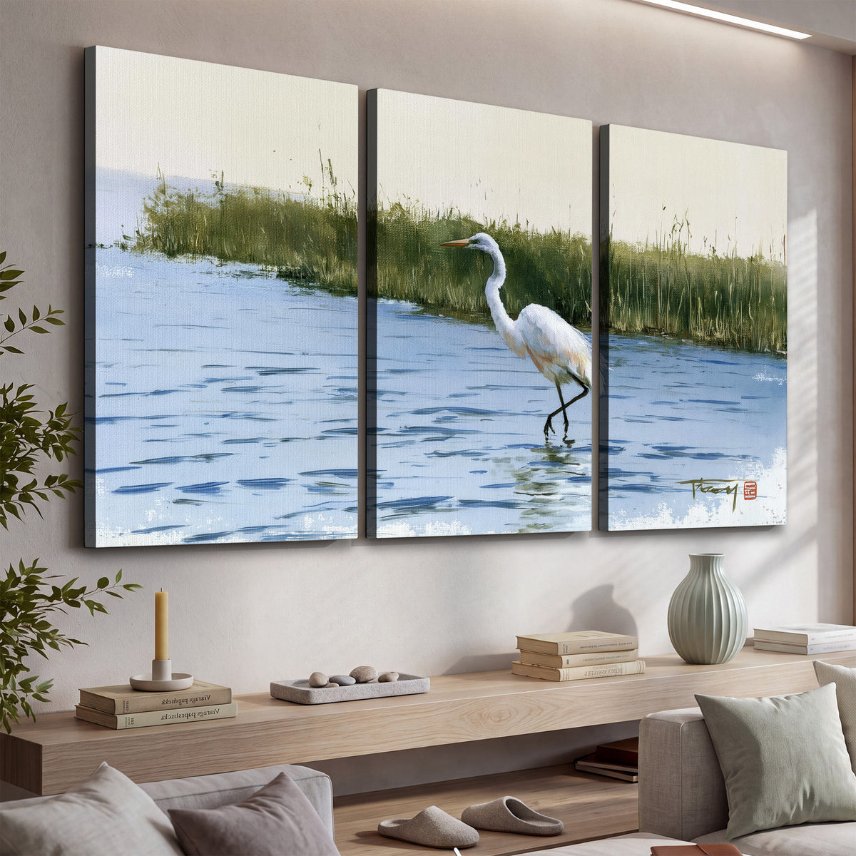 A white heron wading through bright blue water beside green reeds 3 piece canvas wall art displayed in a console