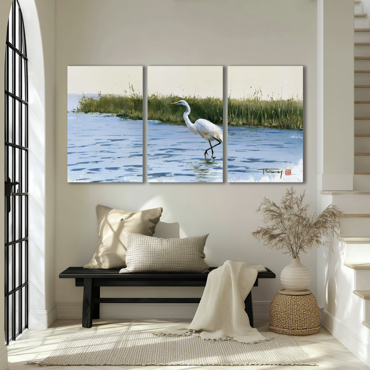 A white heron wading through bright blue water beside green reeds 3 piece canvas wall art displayed in a entryway