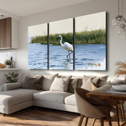 A white heron wading through bright blue water beside green reeds 3 piece canvas wall art room and product view
