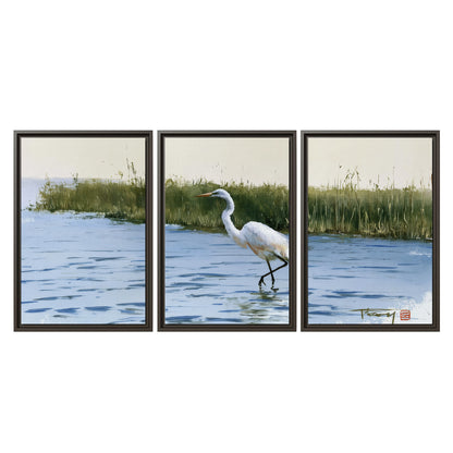 A white heron wading through bright blue water beside green reeds 3 piece framed canvas wall art viewed straight on