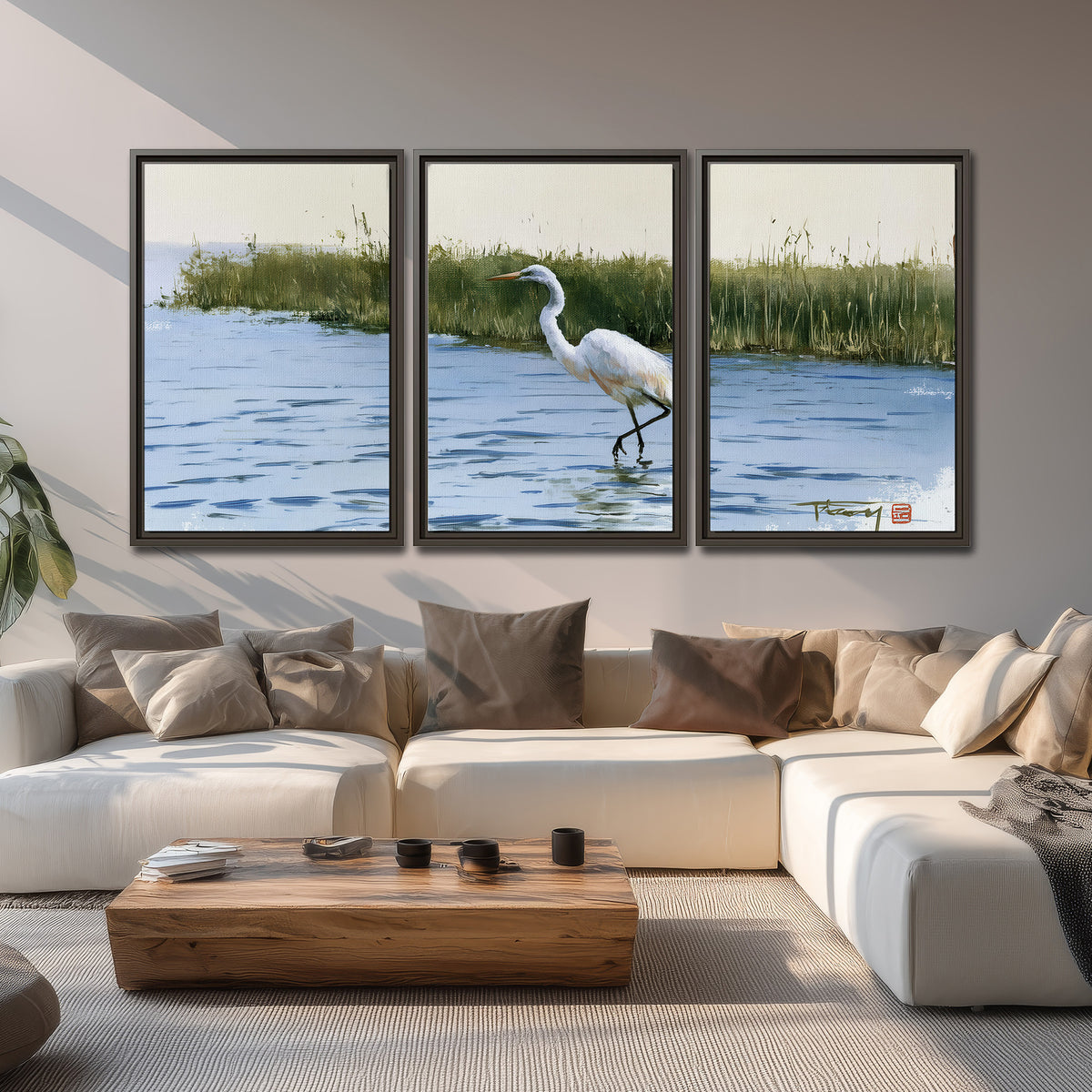 A white heron wading through bright blue water beside green reeds 3 piece framed canvas wall art displayed in a living room
